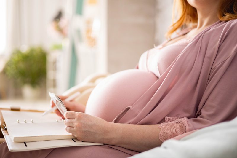 Closeup happy future mother admiring x ray ultrasound photo writing paper diary relaxing on comfortable bed. Relaxed female tummy enjoying pregnancy taking notes ultrasound picture dreaming and hope